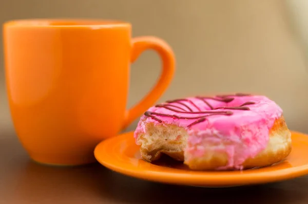 Смачний пончик на помаранчевій тарілці з рожевим глазурованим, з апельсиновою чашкою шоколаду — стокове фото