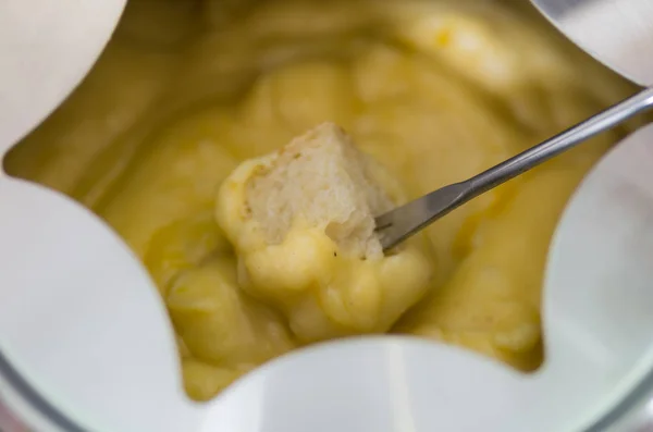 Närbild av en schweizisk fondue gourmetmiddag med ostar och en uppvärmd gryta med ostfondue, man håller med gaffel doppa en bit bröd täcks med ost — Stockfoto