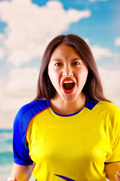 Ecuadoriaanse vrouw dragen van officiële Marathon voetbal shirt staande geconfronteerd met camera, zeer geëngageerde lichaamstaal kijken spel met veel enthousiasme, blauwe hemel en wolken achtergrond — Stockfoto