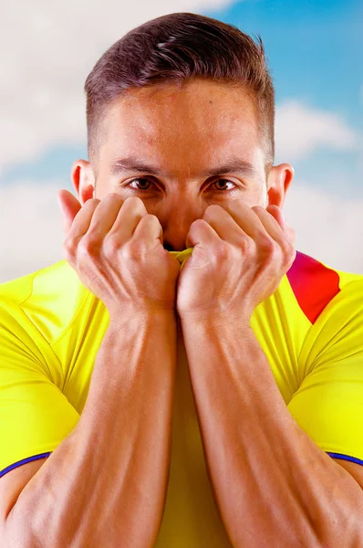 Ecuadoraanse jongeman dragen van officiële Marathon voetbal shirt staande geconfronteerd met camera, zeer geëngageerde lichaamstaal kijken spel met veel enthousiasme, blauwe hemel en wolken achtergrond — Stockfoto