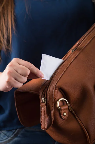 A mão de uma jovem mulher puxando um preservativo para evitar a gravidez de seu bolso de bolsa marrom — Fotografia de Stock