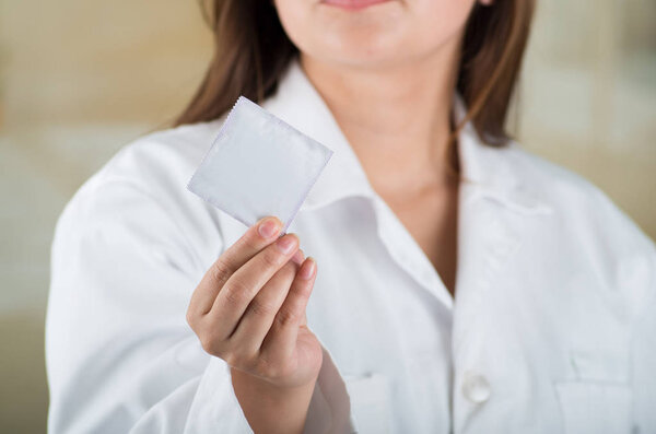 Close up of a doctor holding a male condom package, safe sex concept. Protection against AIDS and birth control