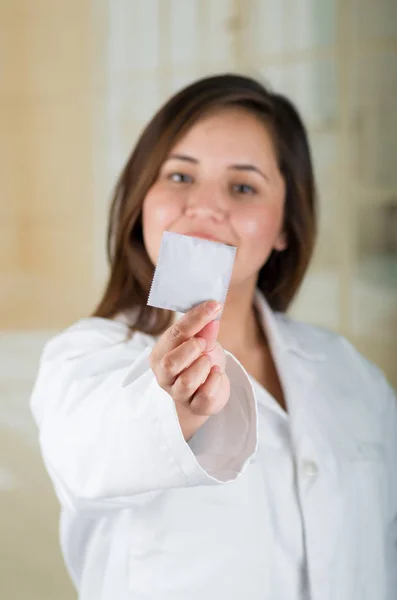 Young beautiful doctor pointing in from of her face a condom package, protection, safe sex concept. Protection against AIDS and birth control — Stock Photo, Image