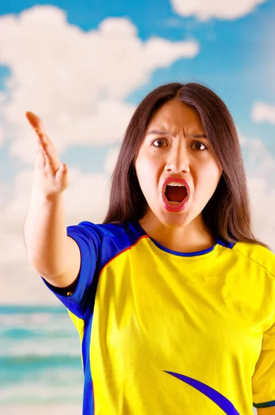 Jeune femme écuadorienne portant une chemise officielle de football Marathon debout face à la caméra, un langage corporel très engagé regardant le jeu avec beaucoup d'enthousiasme, un ciel bleu et un fond nuageux — Photo