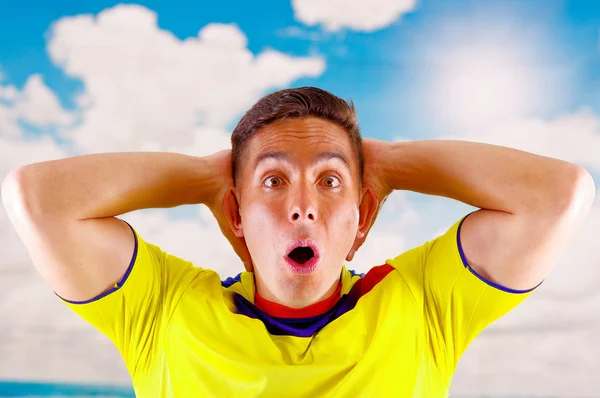 Joven ecuatoriano vistiendo camiseta oficial de fútbol maratón de pie frente a cámara, lenguaje corporal muy comprometido viendo el juego con gran entusiasmo, cielo azul y fondo de nubes — Foto de Stock