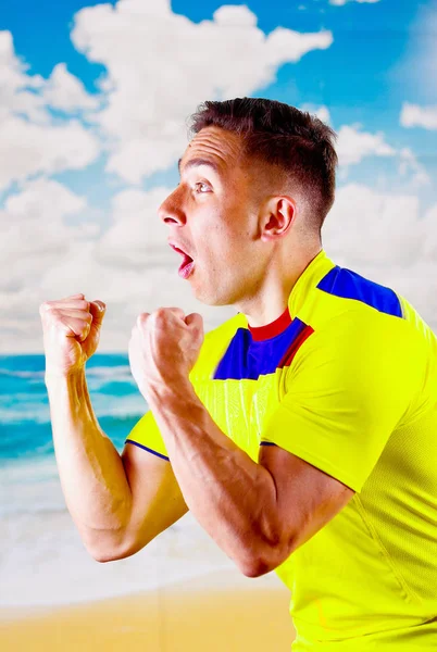 Ecuadoraanse jongeman dragen van officiële Marathon voetbal shirt staande geconfronteerd met camera, zeer geëngageerde lichaamstaal kijken spel met veel enthousiasme, blauwe hemel en wolken achtergrond — Stockfoto