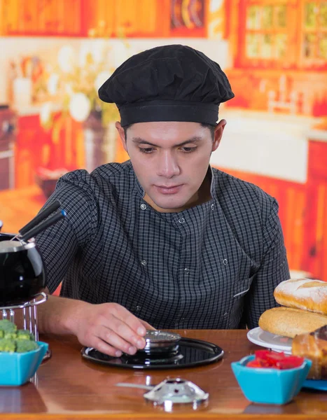 Cheff joven serio preparando una cena gourmet de fondue suiza en mesa de madera en el fondo de la cocina —  Fotos de Stock