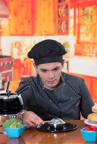 Knappe jonge chef voorbereiding een gastronomische Zwitserse fondue diner op houten tafel in de keuken achtergrond — Stockfoto