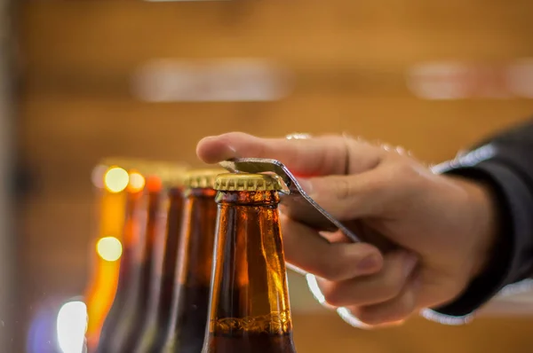 Close up de um homem usando um abridor para as garrafas de cerveja artesanal em fundo borrado — Fotografia de Stock