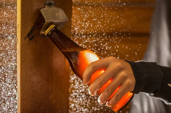 Primer plano de un hombre sosteniendo una botella de cerveza artesanal usando un abridor, sobre fondo de madera — Foto de Stock