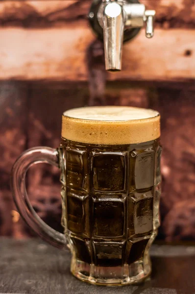 Deliciosa cerveja artesanal escura preenchida em um copo de cerveja na mesa de madeira — Fotografia de Stock