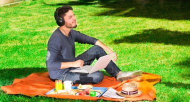 Müzik dinleme ve bir parkta piknik onu giyen kulaklık mutlu genç adam