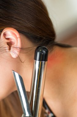 Güzel genç kadın onun curling saç Ütü kullanarak onun omuz yandı