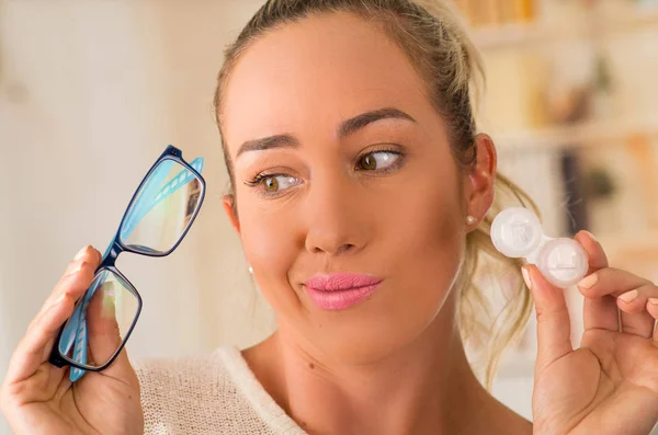 Giovane donna bionda che tiene in mano il caso della lente a contatto e tiene in mano un occhiale blu su sfondo sfocato., concetto di vista e eyecare — Foto Stock