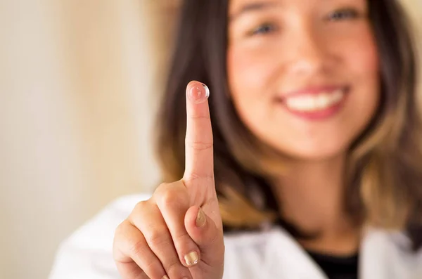 Contactlens op vinger en mooie vrouw die lacht achter op grijze achtergrond — Stockfoto