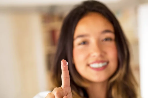 Contactlens op vinger en mooie vrouw die lacht achter op grijze achtergrond — Stockfoto