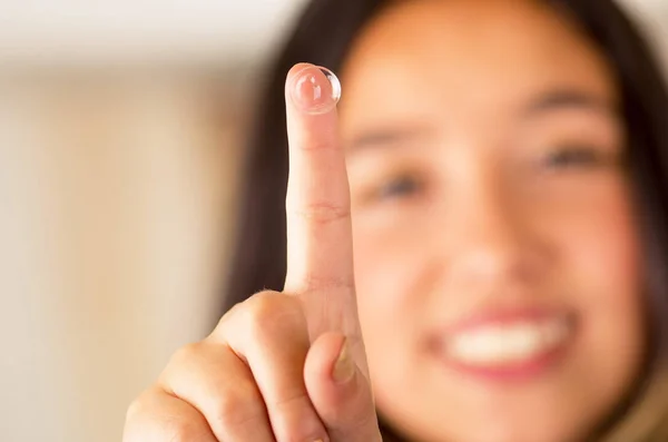 Kontaktlins på finger och vacker kvinna ler bakom på grå bakgrund — Stockfoto
