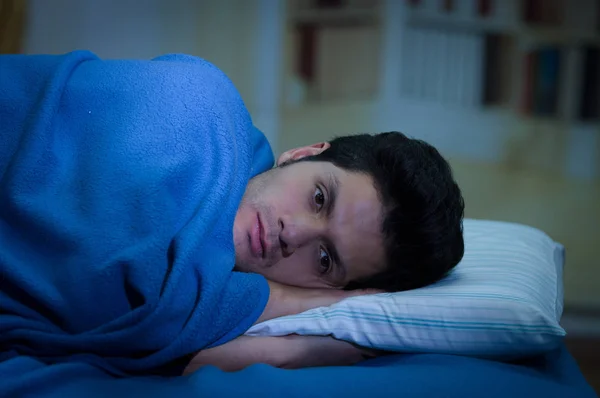 Beau jeune homme au lit avec les yeux ouverts souffrant d'insomnie et de troubles du sommeil en pensant à son problème, fond de la pièce — Photo