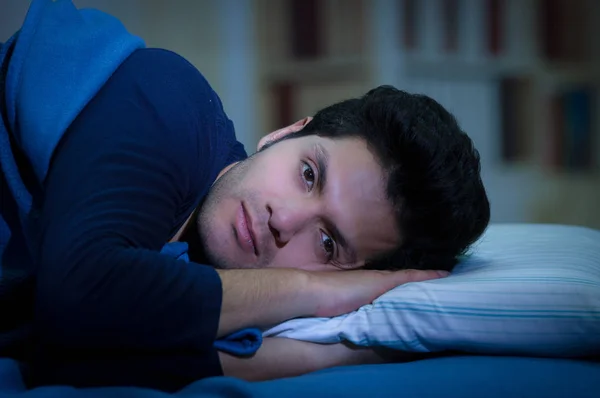 Hombre joven guapo en la cama con los ojos abiertos sufriendo insomnio y trastorno del sueño pensando en su problema, fondo de la habitación —  Fotos de Stock