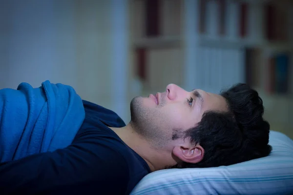 Przystojny młody mężczyzna w łóżku z oczy otwarte, cierpiących na zaburzenia snu i bezsenność, myśląc o swoim problemie, bocznym widokiem w tło pokoju — Zdjęcie stockowe