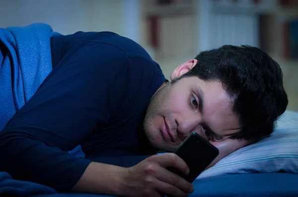 Les hommes toxicomanes des médias sociaux sur le lit ne dorment pas parce que jouer téléphone intelligent, fond de la chambre — Photo