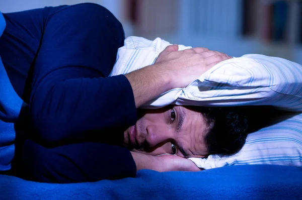 Bello giovanotto a letto con gli occhi aperti soffre di insonnia e disturbi del sonno pensando al suo problema coprirsi la testa con un cuscino, sfondo stanza — Foto Stock