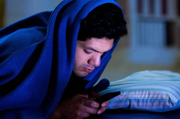 Les hommes toxicomanes des médias sociaux sur le lit ne dorment pas parce que jouer téléphone intelligent, couvrant sa tête avec une couverture bleue, fond de la chambre — Photo