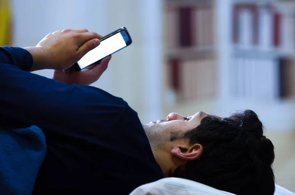 Les hommes toxicomanes des médias sociaux sur le lit ne dorment pas parce que jouer téléphone intelligent, fond de la chambre — Photo