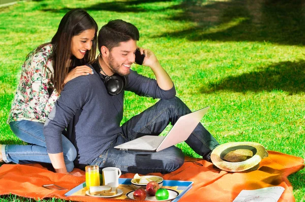 Junges glückliches Paar genießt Picknick im Park, während der Kerl sein Handy benutzt — Stockfoto