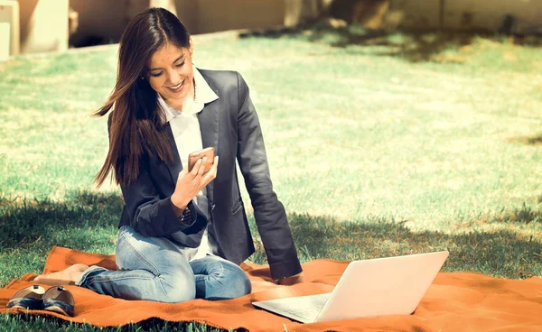 Menina jovem e feliz com laptop no parque usando seu celular, efeito vintage — Fotografia de Stock