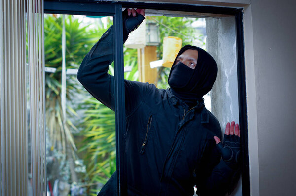 Грабитель пытается разбить окно, чтобы войти в дом
