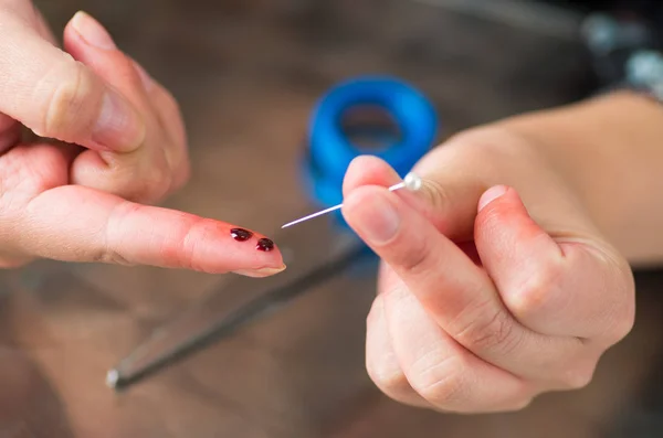 Young woman injured bleeding finger closeup with a needle — Stock Photo, Image