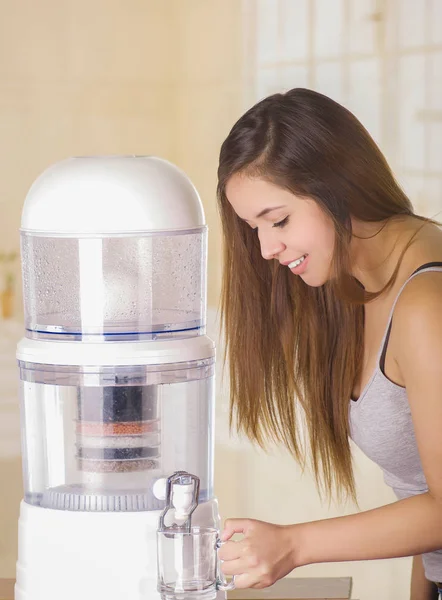 Schöne lächelnde Frau, die ein Glas Wasser füllt, mit einem Filtersystem des Wasserreinigers auf einem Hintergrund in der Küche — Stockfoto