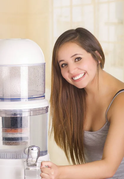 부엌 배경에 정수기의 필터 시스템 물, 잔을 채우는 아름 다운 웃는 여자 — 스톡 사진