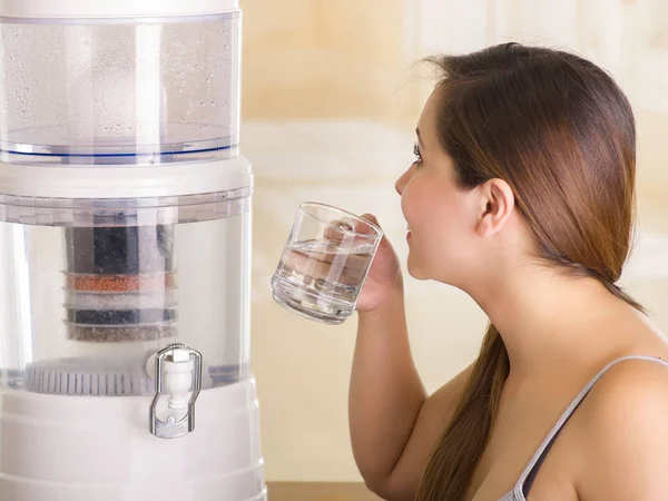 Close up van een mooie vrouw, drinken van een glas water met een systeem van de filter van water purifier op de achtergrond van een keuken — Stockfoto