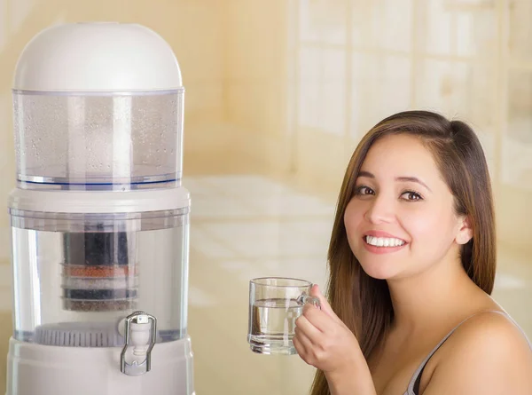キッチンの背景に浄水器のフィルター システムと水のガラスを保持して笑顔美人のクローズ アップ — ストック写真
