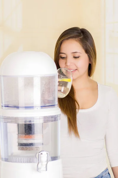 Mooie vrouw, drinken van een glas water met een systeem van de filter van water purifier op de achtergrond van een keuken — Stockfoto
