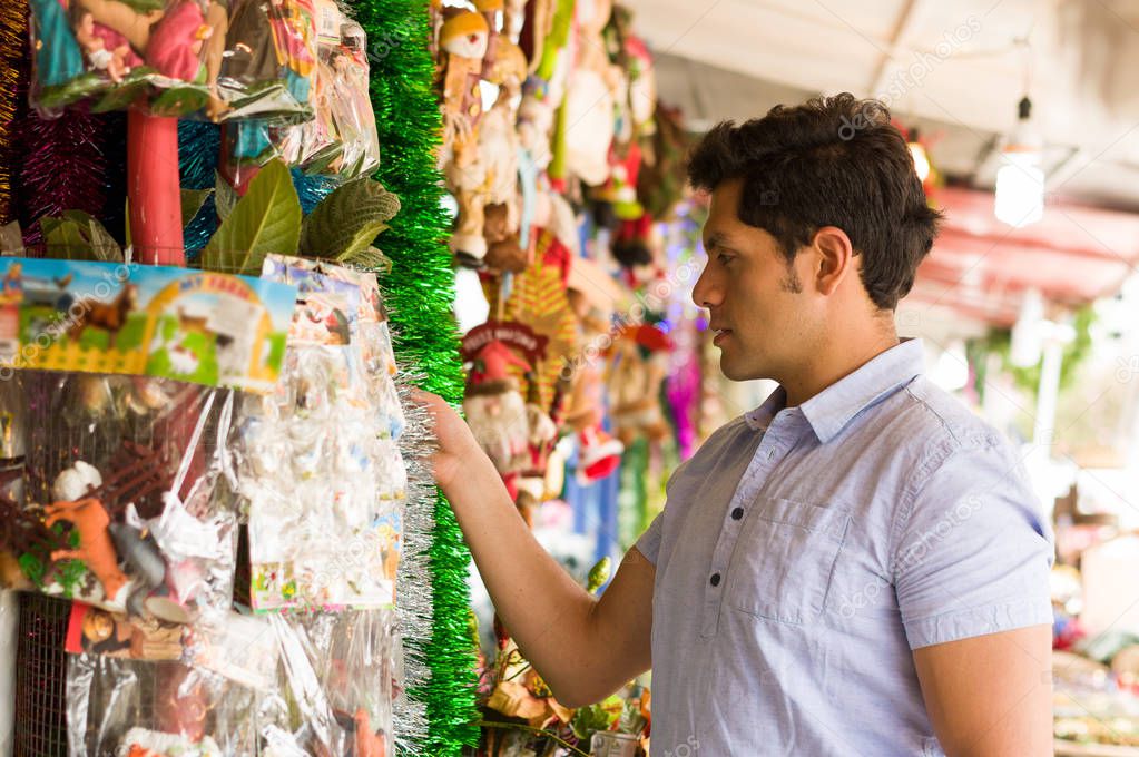 Handsome young man watching beautiful and colorful christmas tree decoration in a market