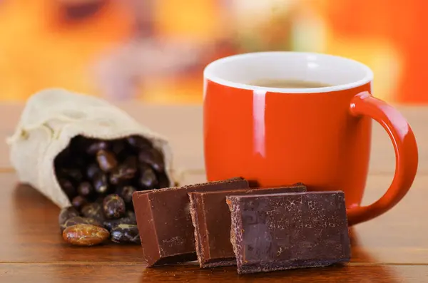 Fagiolo di cacao secco in un piccolo sacco e una tazza di cioccolato su uno sfondo di legno — Foto Stock