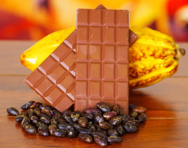 Close up of a fresh cocoa pods, chocolate bar and dry cocoa beans over a wooden table — Stock Photo, Image