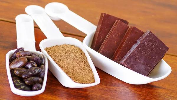 Fagiolo di cacao secco scuro, pezzi di cioccolato e cacao in polvere all'interno di uno scoop retrò bianco su sfondo di legno — Foto Stock