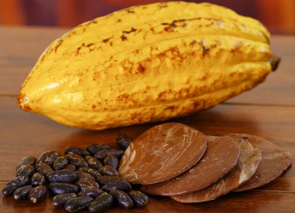Fresh cocoa pods and dark dry cocoa bean with some pieces of dark chocoloate over a wooden background — Stock Photo, Image