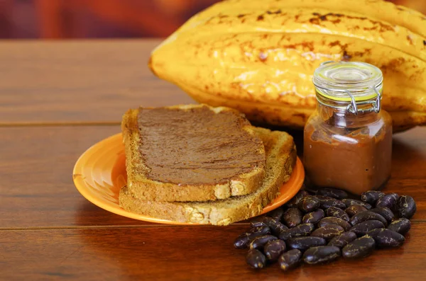 Fresh cocoa pods and dry cocoa beans, and cocoa cream over pieces of bread — Stock Photo, Image