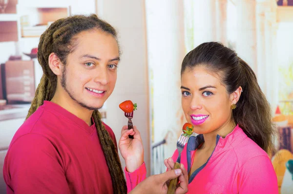 Casal saudável jovem hispânico desfrutando de café da manhã juntos, compartilhando morangos e sorrindo, casa cozinha fundo — Fotografia de Stock