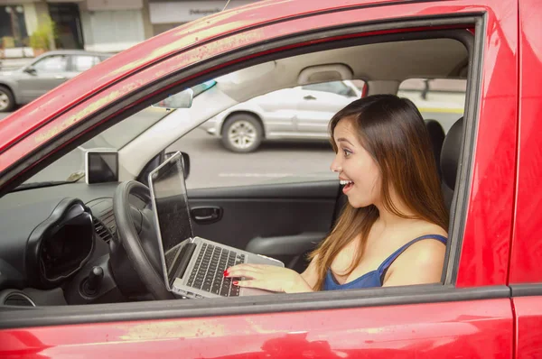 Schöne lächelnde junge Frau, die an ihrem Computer arbeitet, während das Auto von allein fährt — Stockfoto