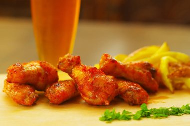 Bir bardak bira ve ahşap tahta üzerinde arkasında Fransız kızartması ile lezzetli ızgara tavuk kanatları