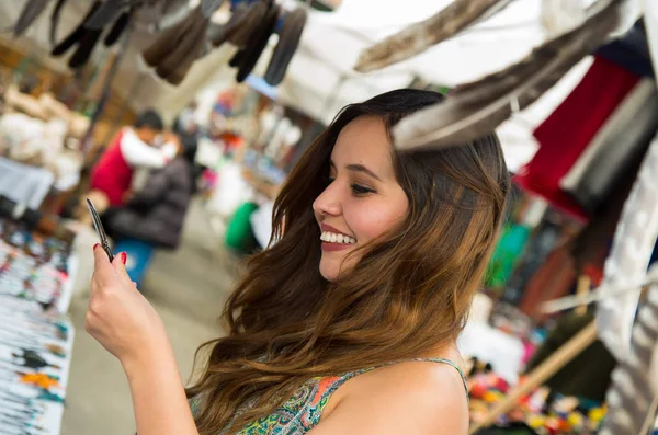 Belle femme souriante tenant quelque chose dans sa main dans les vêtements traditionnels andins et de l'artisanat avec une plume floue devant, fond du marché — Photo