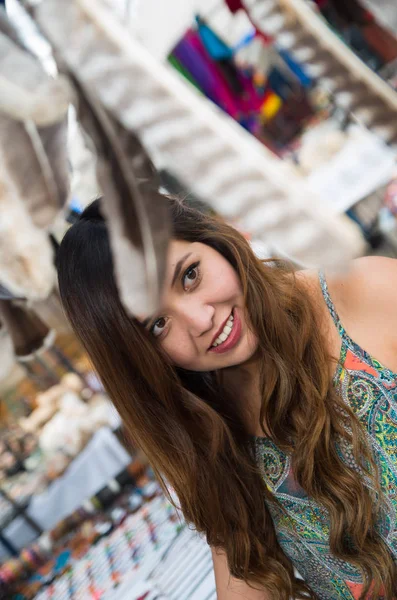 Krásná žena hledá něco v andské tradiční oděvy a řemesel s rozmazané pírko vpředu, na trhu pozadí — Stock fotografie