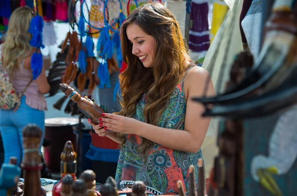 Mujer joven sosteniendo en sus manos una artesanía andina, con un fondo de telas — Foto de Stock