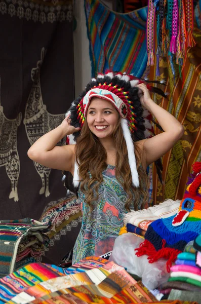 Una hermosa joven con plumas de sombrero nativo americano. con telas de colores de fondo — Foto de Stock